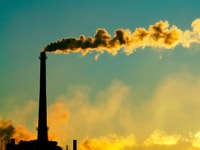 CO2 Steam rises smokestack factory silhouetted against sunlight