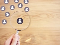 Human resources management and recruitment concept, Hand holding magnifying glass search people paper icon on top desk._1124554700