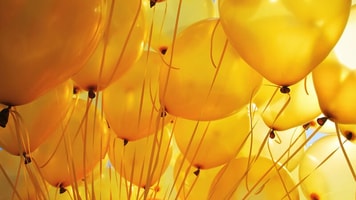 Helium-Background-of-bright-yellow-inflatable-balloons-up-in-the-air-backlit-by-sun