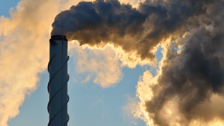 Factory pipe close-up with a lot of smoke against blue sky